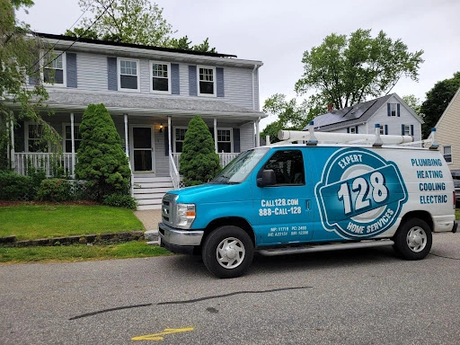 A blue service van labeled "128 Expert Home Services" is parked in front of a suburban house. The services listed on the van include plumbing, heating, cooling, and electric.